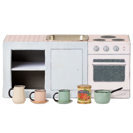 Miniature toy kitchen set with a pink countertop, mini sink, stovetop, and oven. In front are colorful cups, a can of tomatoes, and a small saucepan. Charming and playful.