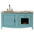 A miniature blue kitchen set with a sink, faucet, and stovetop. An oven with a glass door shows a pie inside. The tone is playful and nostalgic.