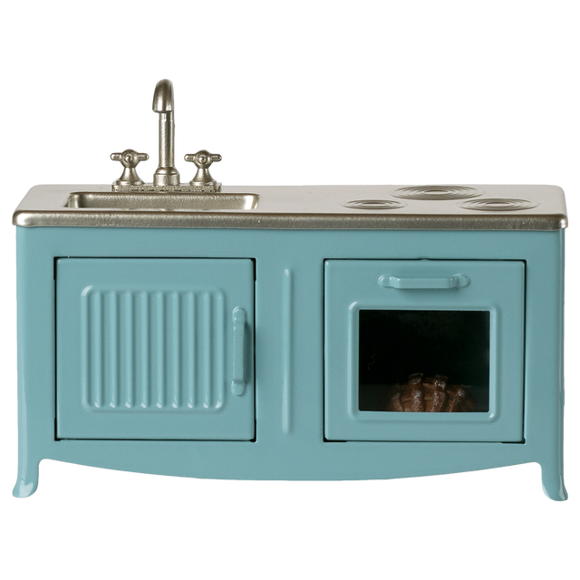 A miniature blue kitchen set with a sink, faucet, and stovetop. An oven with a glass door shows a pie inside. The tone is playful and nostalgic.
