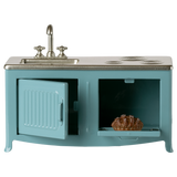 A miniature blue kitchen set with a silver sink and stove. The oven door is open, revealing a small baked pie inside. The simplicity evokes a playful mood.