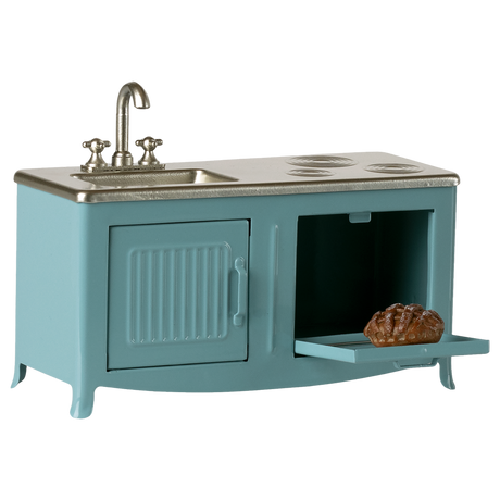 A miniature blue kitchen with a silver sink and stove. The open oven door reveals a small loaf of bread. The scene conveys a playful, retro vibe.