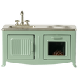 A miniature vintage kitchen set in pale green with a silver faucet and stove. It includes a sink, oven with a glass door, and a visible brown pie inside.