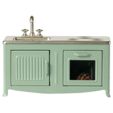 A miniature vintage kitchen set in pale green with a silver faucet and stove. It includes a sink, oven with a glass door, and a visible brown pie inside.