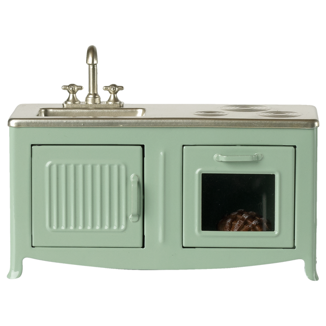 A miniature vintage kitchen set in pale green with a silver faucet and stove. It includes a sink, oven with a glass door, and a visible brown pie inside.