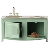 A miniature vintage kitchen set in pale green with a silver faucet and stove. It includes a sink, oven with a glass door, and a visible brown pie inside.