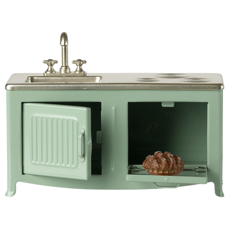 A miniature vintage kitchen set in pale green with a silver faucet and stove. It includes a sink, oven with a glass door, and a visible brown pie inside.