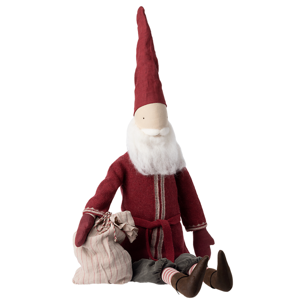 A toy gnome sits with its legs extended. It wears a tall red hat and matching coat, holding a striped sack. The gnome has a white beard.