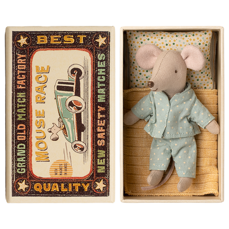 Toy mouse in blue pajamas lies in a matchbox, resembling a cozy bed. The box has vintage-style "Mouse Race" label. Cute and nostalgic.