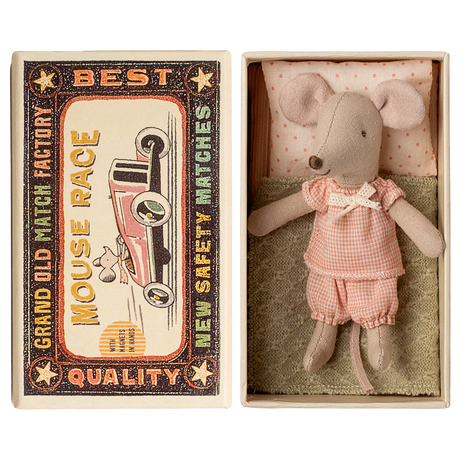 Toy mouse in pink clothes lies in an open matchbox, with vintage race car graphics on the lid. The scene has a nostalgic and whimsical feel.