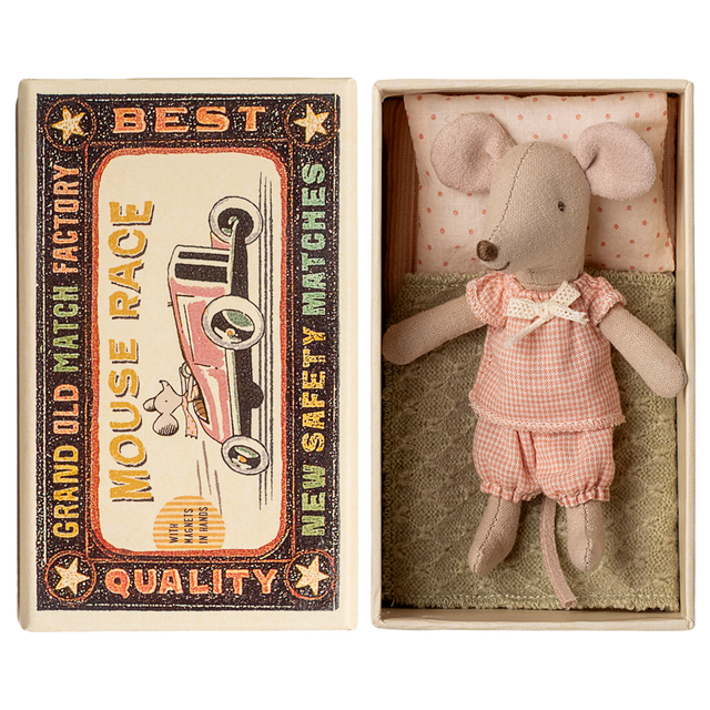Toy mouse in pink clothes lies in an open matchbox, with vintage race car graphics on the lid. The scene has a nostalgic and whimsical feel.
