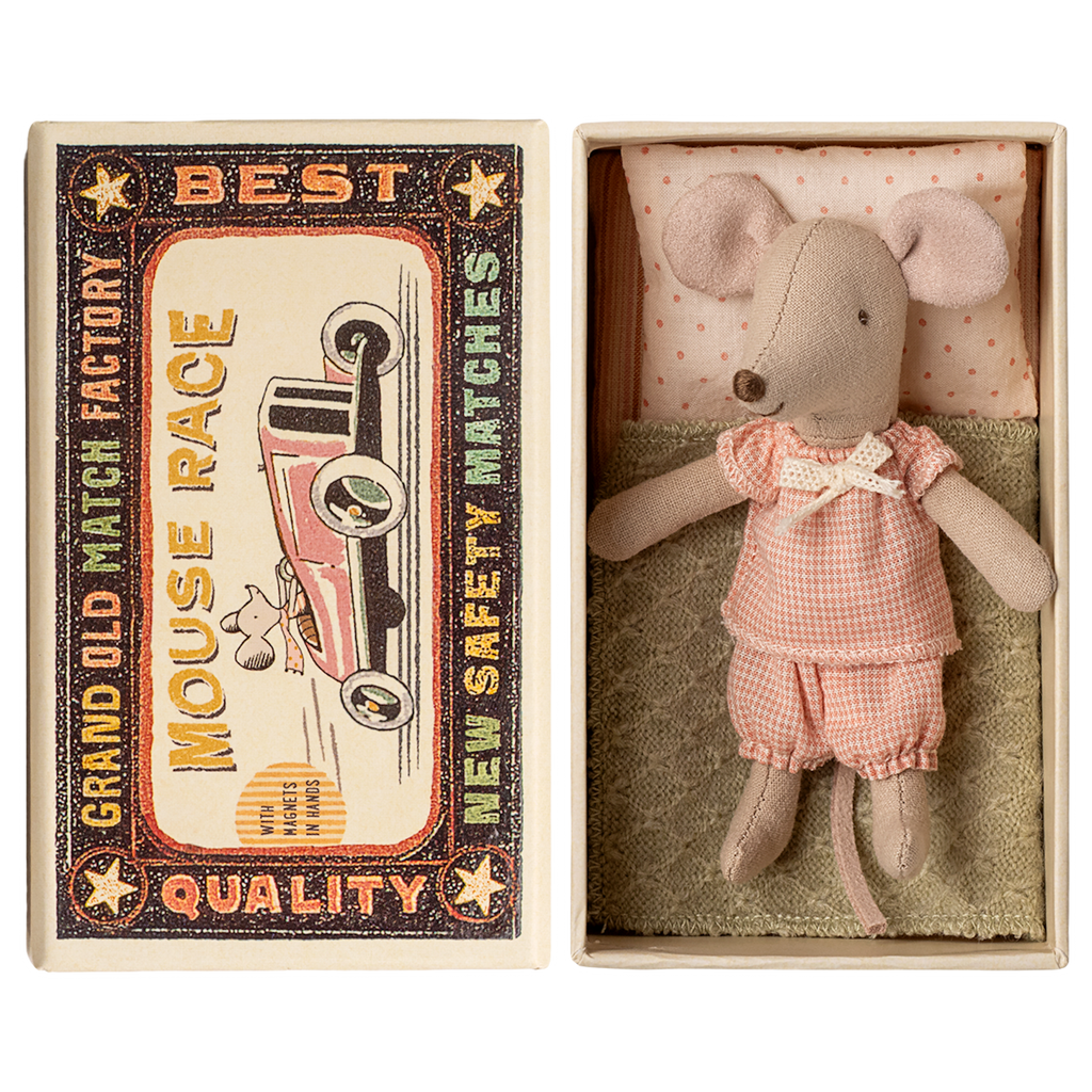 Toy mouse in pink clothes lies in an open matchbox, with vintage race car graphics on the lid. The scene has a nostalgic and whimsical feel.