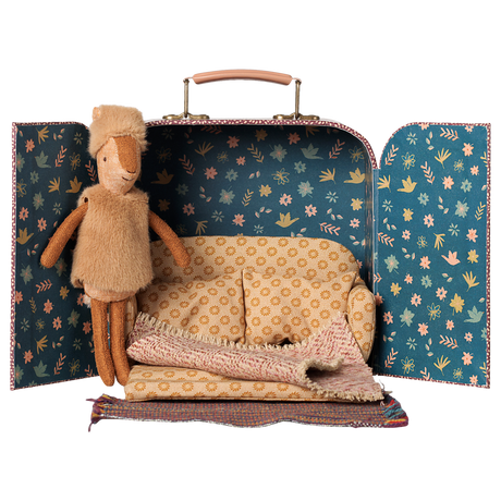 Maileg little sister reindeer plush doll inside a toy suitcase dollhouse with a miniature sofa.