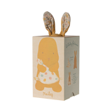A soft, brown stuffed bunny with patterned fabric ears sits holding a white, polka-dotted blanket. The cozy scene conveys warmth and comfort.
