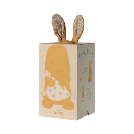 A soft, brown stuffed bunny with patterned fabric ears sits holding a white, polka-dotted blanket. The cozy scene conveys warmth and comfort.