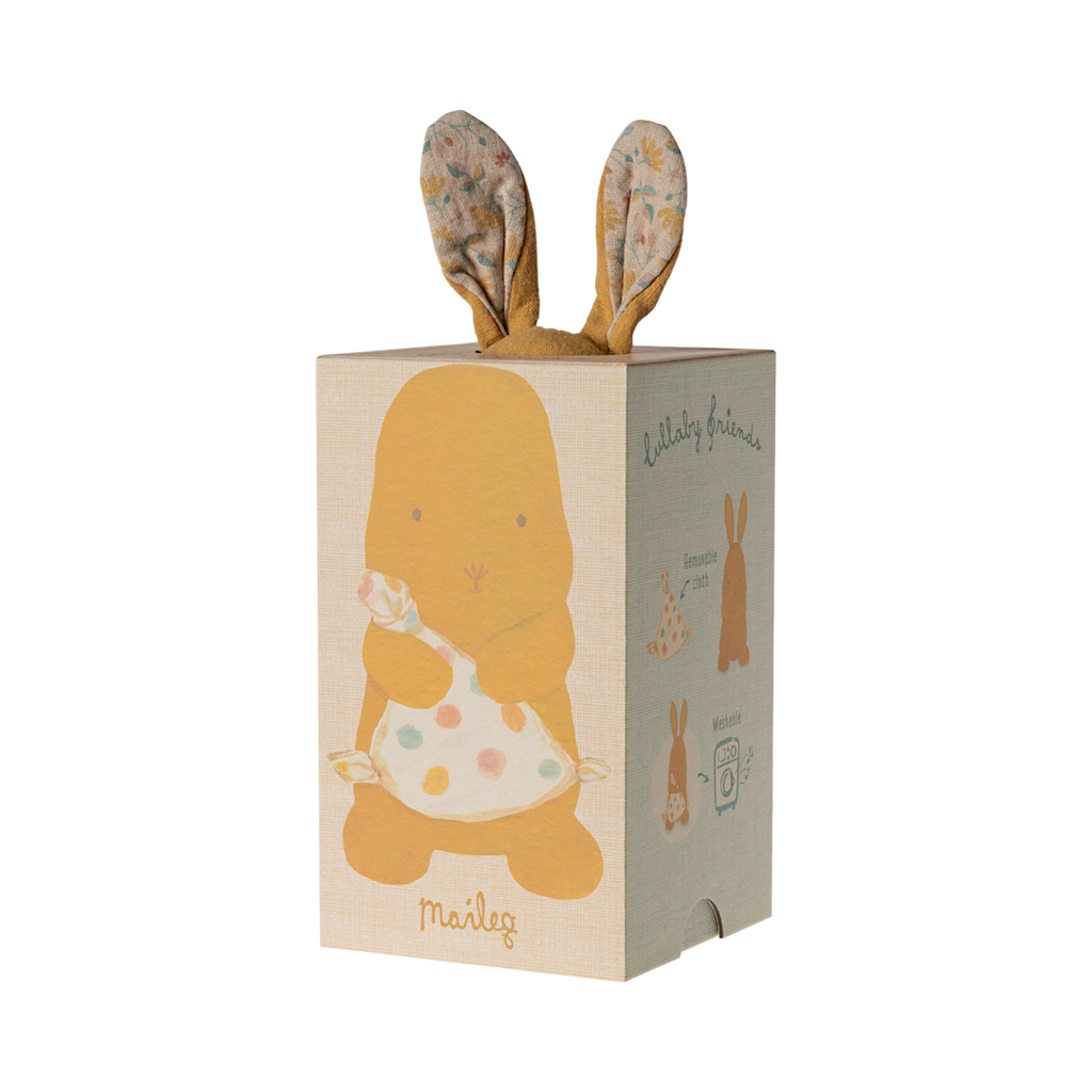 A soft, brown stuffed bunny with patterned fabric ears sits holding a white, polka-dotted blanket. The cozy scene conveys warmth and comfort.