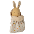 A soft toy rabbit with embroidered features and patterned ears is wrapped in a cream polka dot fabric. The tone is cozy and whimsical.