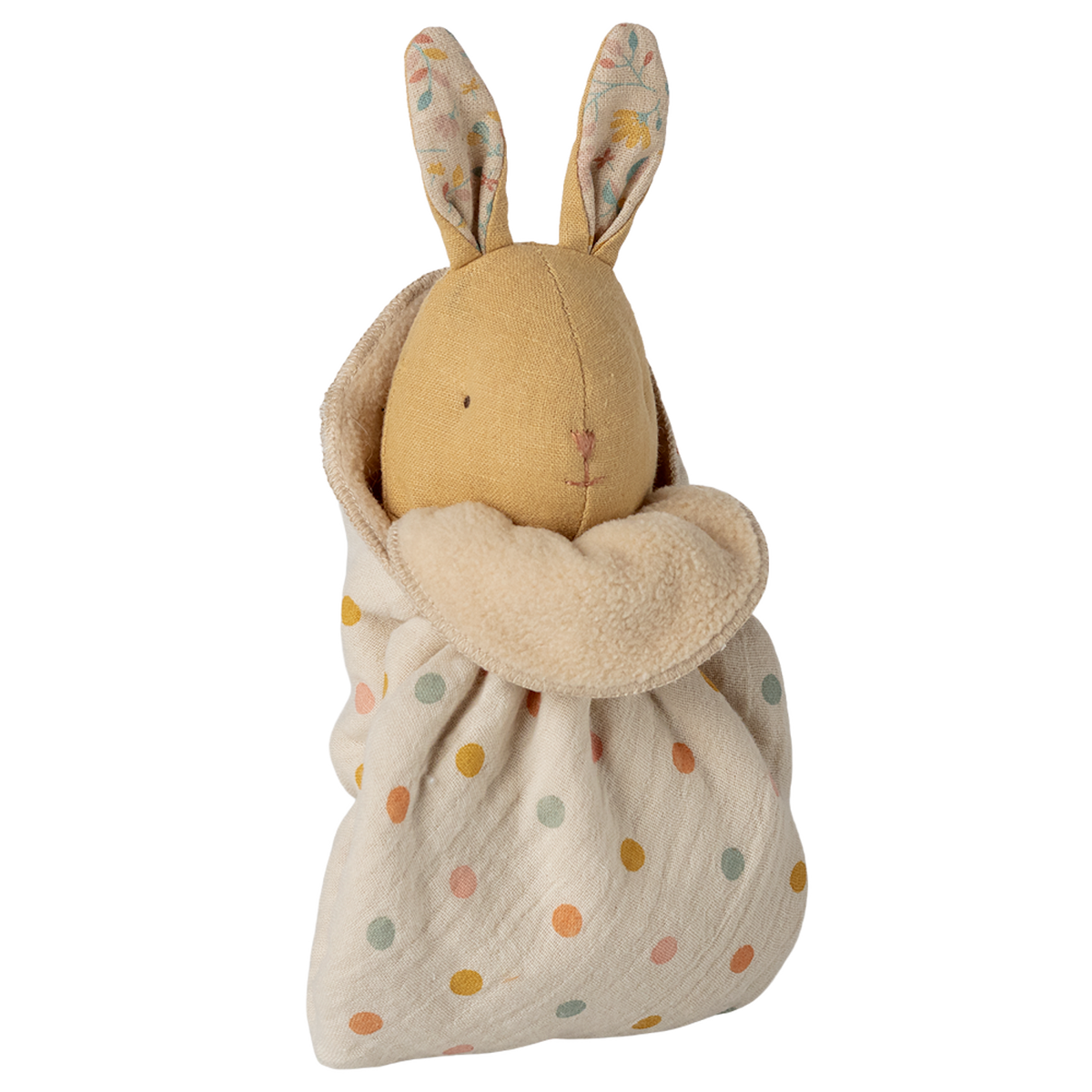 A soft toy rabbit with embroidered features and patterned ears is wrapped in a cream polka dot fabric. The tone is cozy and whimsical.