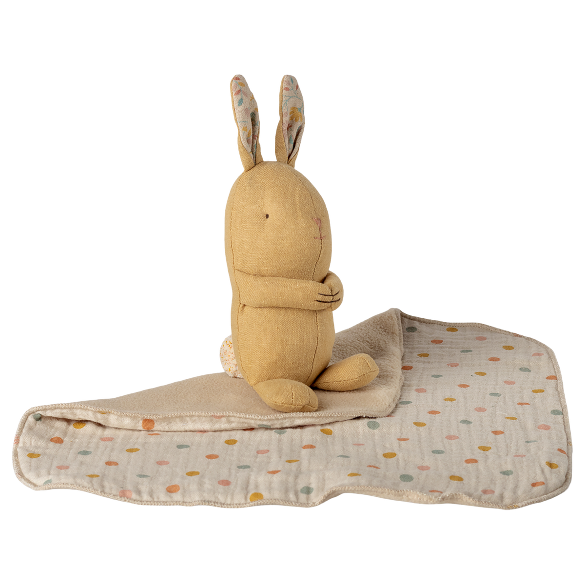 A soft, beige stuffed rabbit with folded arms and patterned ears sits on a quilt with pastel polka dots. The background is white, creating a cozy, serene feel.