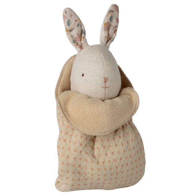 A plush toy rabbit with floral-patterned ears and an embroidered face is snugly swaddled in a soft, polka-dotted beige blanket, set against a white background.