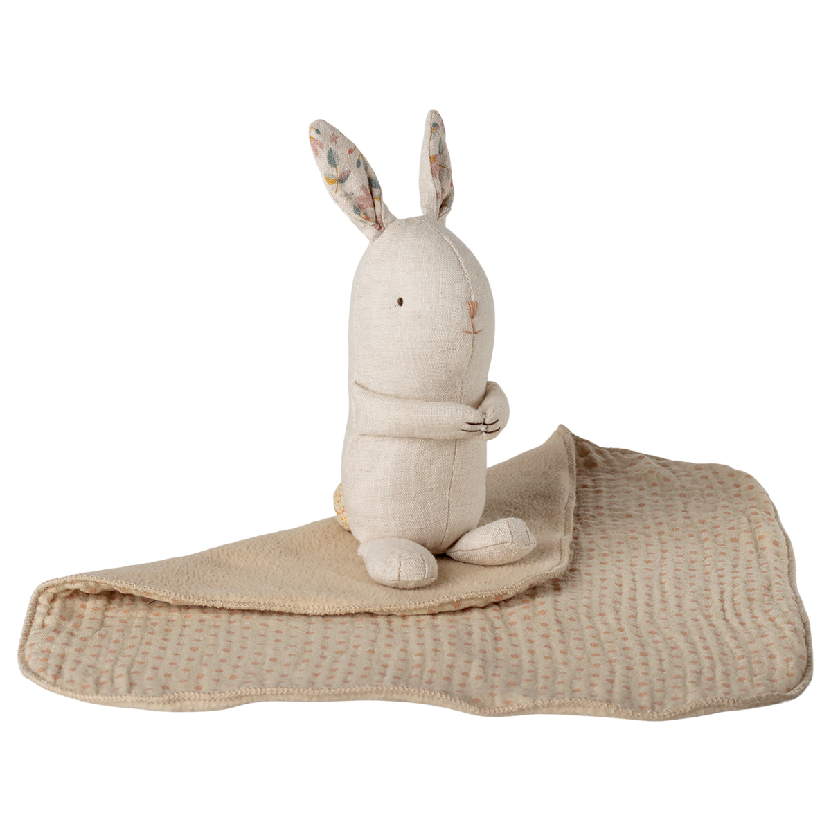 A beige fabric bunny with floral inner ears sits on a soft, patterned blanket against a white background, conveying a cozy, comforting tone.