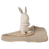 A beige fabric bunny with floral inner ears sits on a soft, patterned blanket against a white background, conveying a cozy, comforting tone.