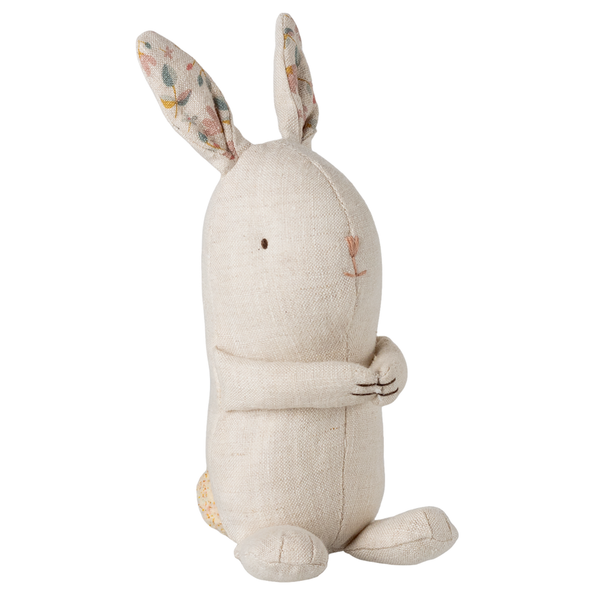 A beige fabric bunny toy sits upright against a white background. It features long ears with floral patterns inside, a simple embroidered face, and a friendly, serene expression.