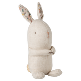 A beige fabric bunny toy sits upright against a white background. It features long ears with floral patterns inside, a simple embroidered face, and a friendly, serene expression.