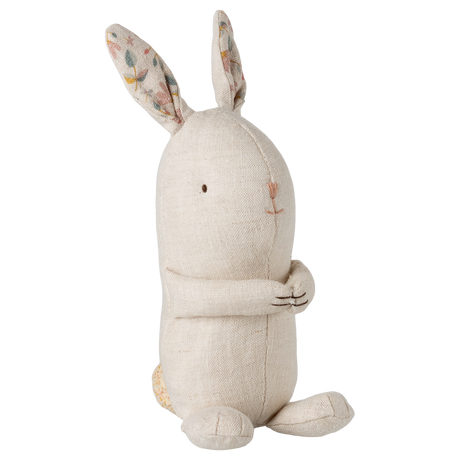 A beige fabric bunny toy sits upright against a white background. It features long ears with floral patterns inside, a simple embroidered face, and a friendly, serene expression.