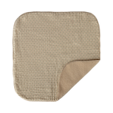 A beige, square sherpa burp cloth with a subtle grid pattern lies on a white background. One corner is folded, showing a fluffy inner lining.