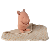 A soft pink stuffed animal resembling a small rodent sits on a beige blanket with brown polka dots, set against a white background. The tone is cozy.