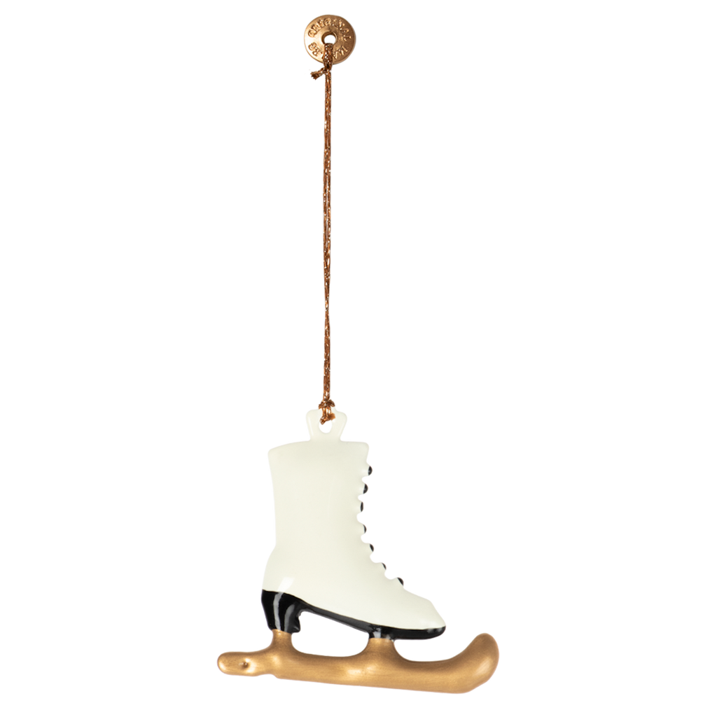 A small, white ice skate ornament with black accents and a golden blade hangs from a string, set against a solid white background.