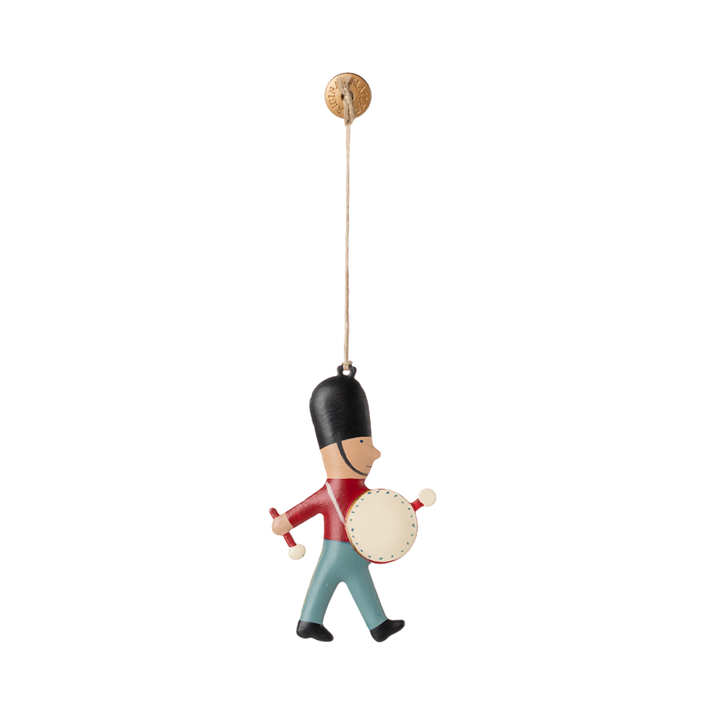 A hanging ornament of a toy soldier wearing a tall black hat, red jacket, and blue pants, playing a drum. The toy is suspended by a string, conveying a playful and cheerful tone.