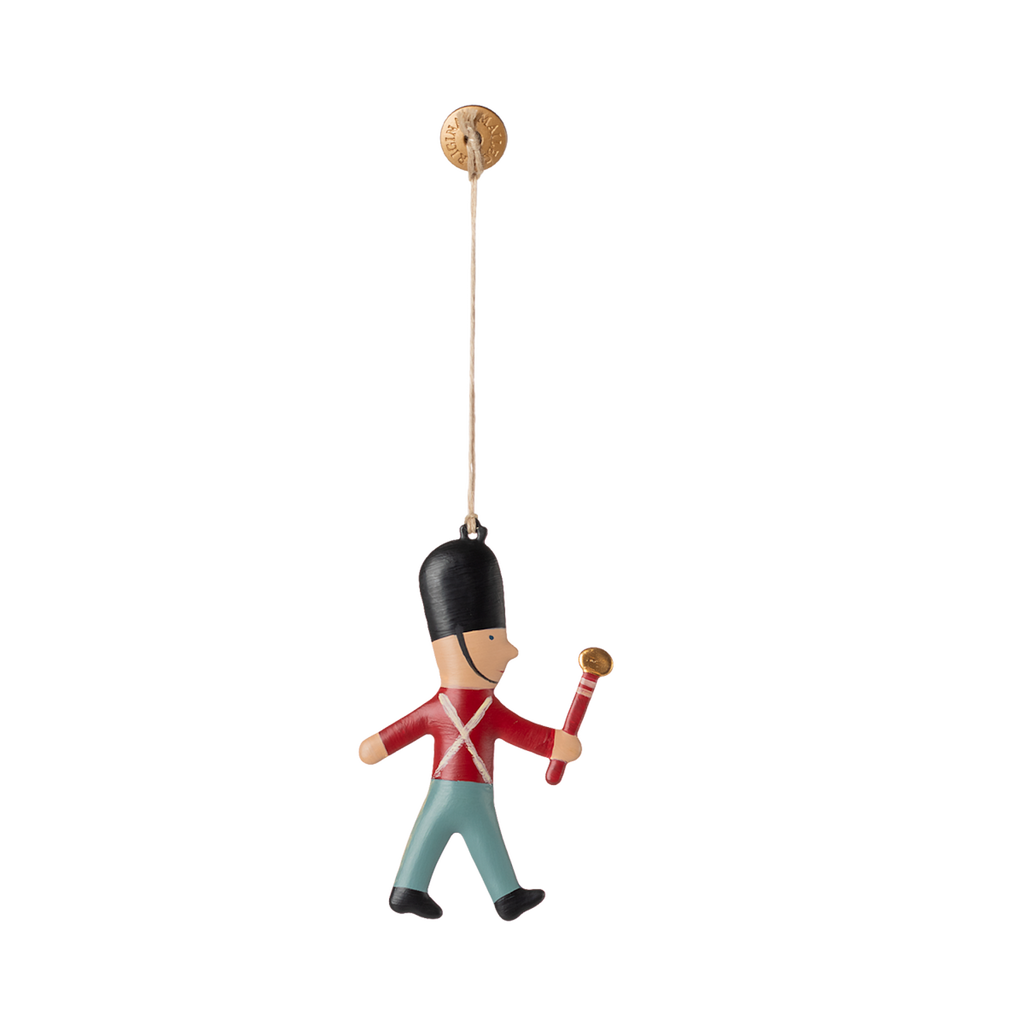 Toy soldier ornament hanging by a string. The soldier wears a black hat, red coat, and blue pants, holding a red baton. Simple, playful design.