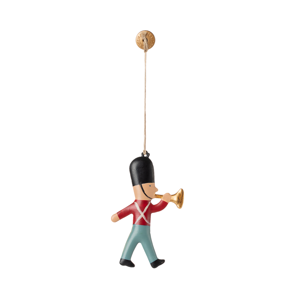 A whimsical ornament of a soldier playing a trumpet, dressed in red and blue, hanging from a gold hook.