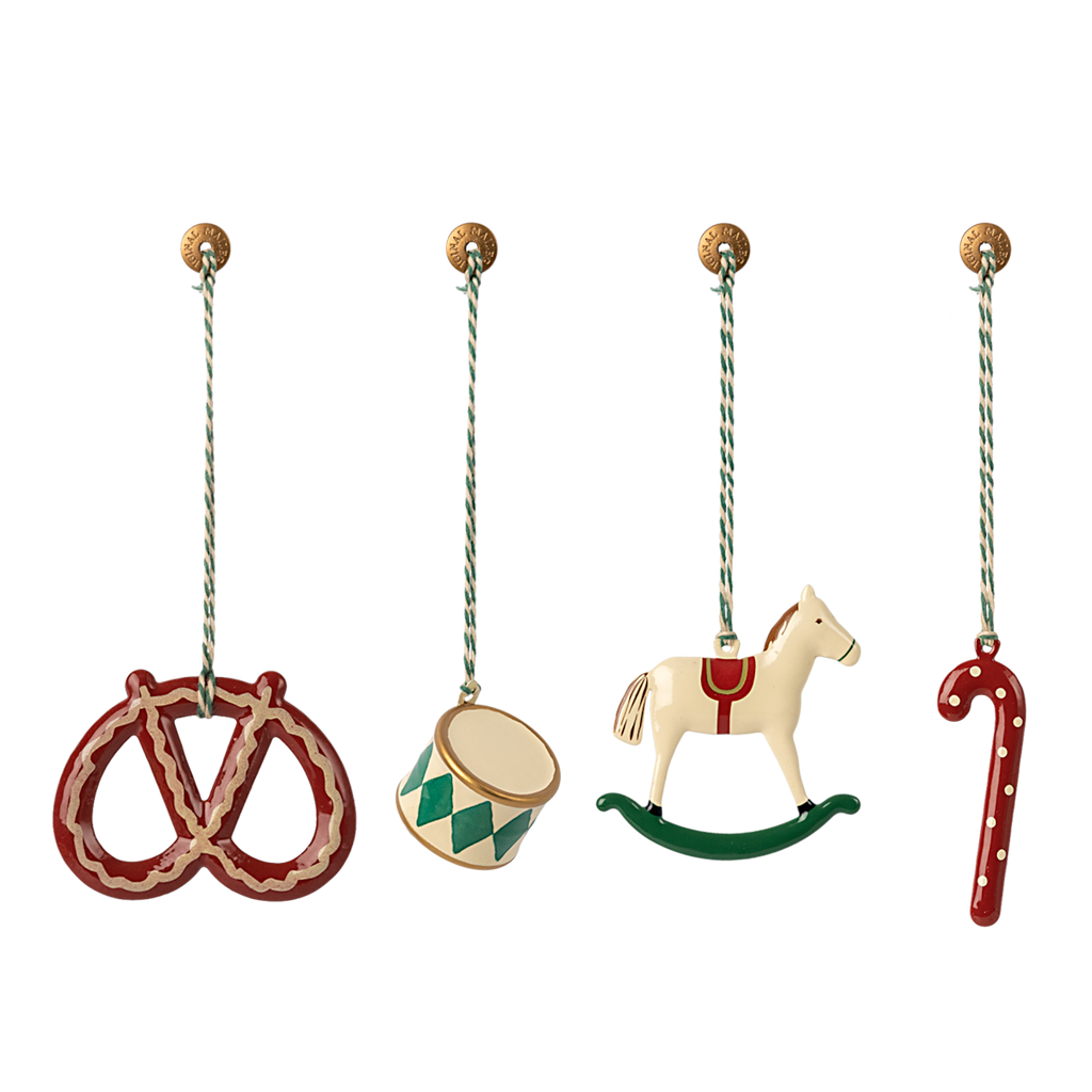 Four hanging ornaments: a red pretzel, a green and white drum, a white rocking horse with red details, and a red candy cane with white dots, each on a string against a white background.