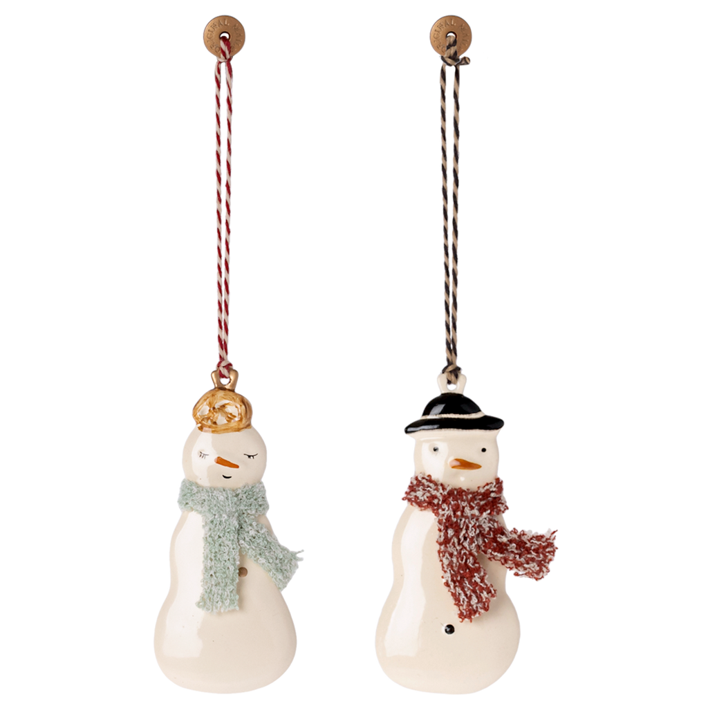 Two ceramic snowman ornaments hang against a white background. One wears a gold hat with a blue scarf, the other a black hat with a red scarf. Festive and whimsical.