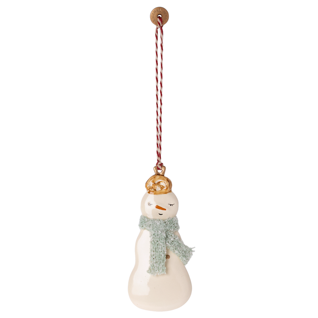 Ceramic snowman ornament with a gold hat and blue scarf, hanging by a red-and-white string. Its simple facial features evoke a playful, cozy vibe.
