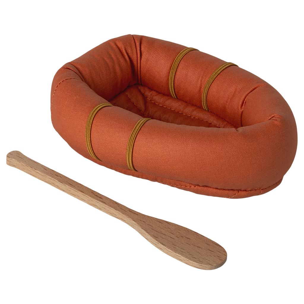 A small, orange, oval-shaped fabric raft with three brown bands is placed on a white background. Beside it lies a simple wooden paddle.