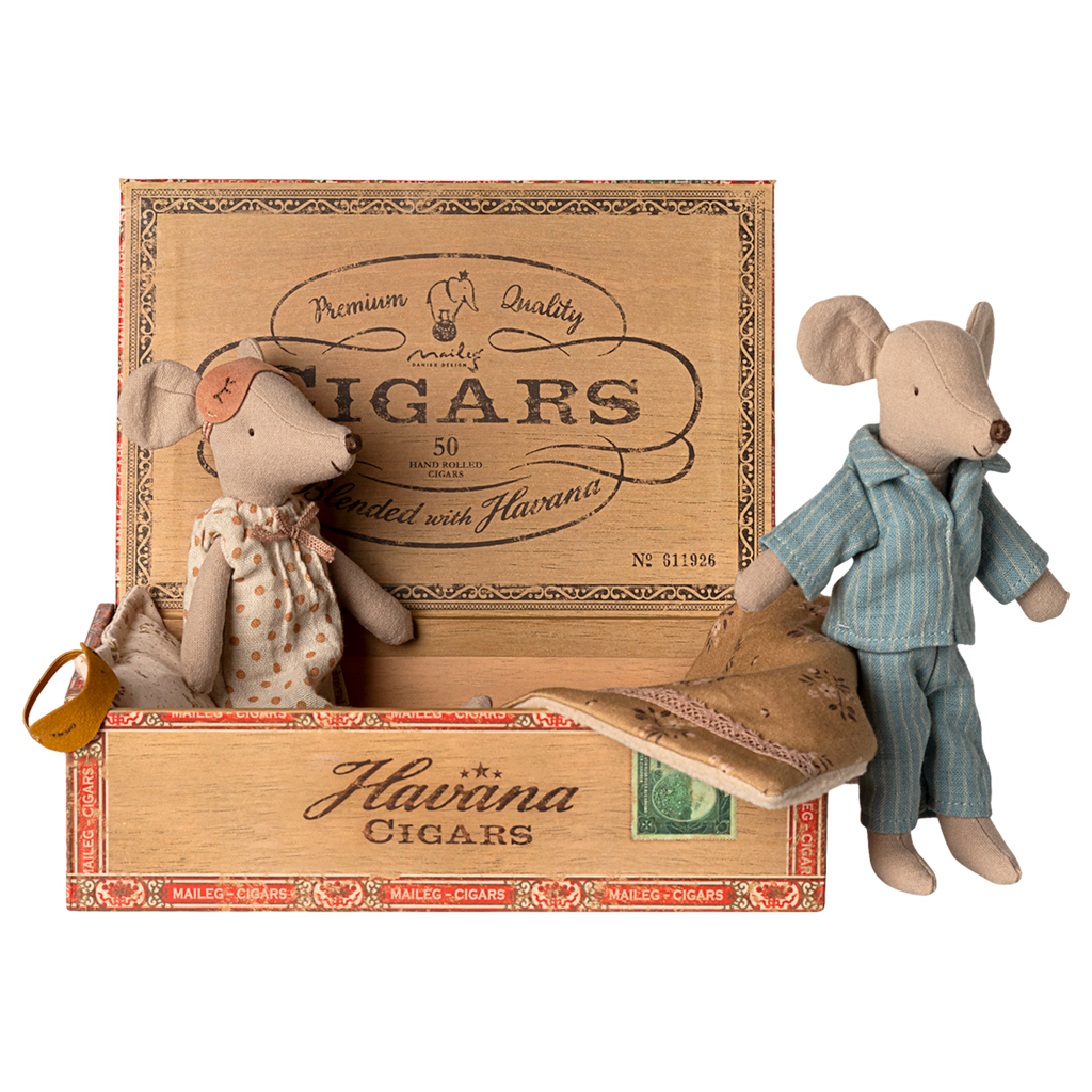 Two toy mice in pajamas rest in a cigar box, one in a polka-dot gown and mask, the other in blue stripes. The mood is cozy and nostalgic.