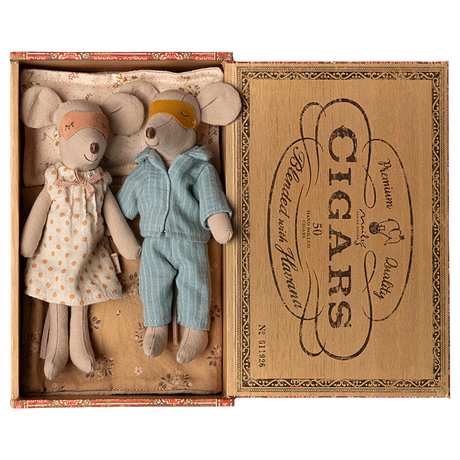 Two toy mice in pajamas rest in a cigar box, one in a polka-dot gown and mask, the other in blue stripes. The mood is cozy and nostalgic.