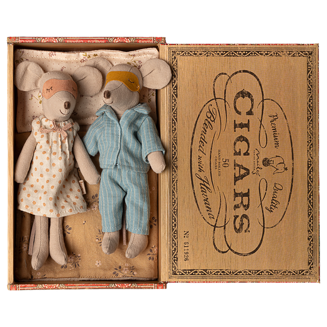 Two toy mice in pajamas rest in a cigar box, one in a polka-dot gown and mask, the other in blue stripes. The mood is cozy and nostalgic.