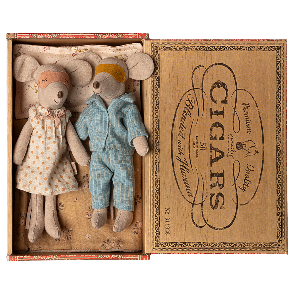 Two toy mice in pajamas rest in a cigar box, one in a polka-dot gown and mask, the other in blue stripes. The mood is cozy and nostalgic.