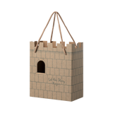 Cardboard gift bag shaped like a castle with a crenelated top. It features a cutout window and the words "Let the Story Begin" printed on it.
