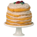 A tall, layered cake with textured icing stands on a white pedestal. Topped with colorful decorative fruits, it sits against a white background.