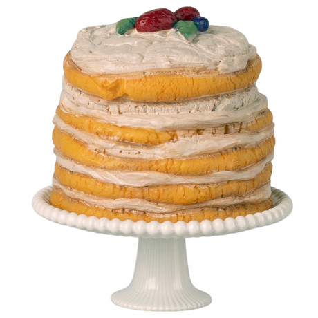 A tall, layered cake with textured icing stands on a white pedestal. Topped with colorful decorative fruits, it sits against a white background.