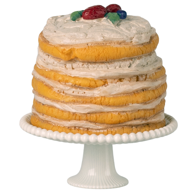 A tall, layered cake with textured icing stands on a white pedestal. Topped with colorful decorative fruits, it sits against a white background.