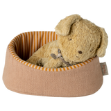 A plush, tan-colored stuffed dog rests peacefully in a small, round pet bed with orange and cream stripes, creating a cozy and serene atmosphere.