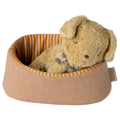A plush, tan-colored stuffed dog rests peacefully in a small, round pet bed with orange and cream stripes, creating a cozy and serene atmosphere.