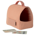 A soft, peach-colored pet carrier with a red grid pattern and handle. Nearby are a Pet Journal and dog stickers against a white background, conveying a cozy, playful vibe.