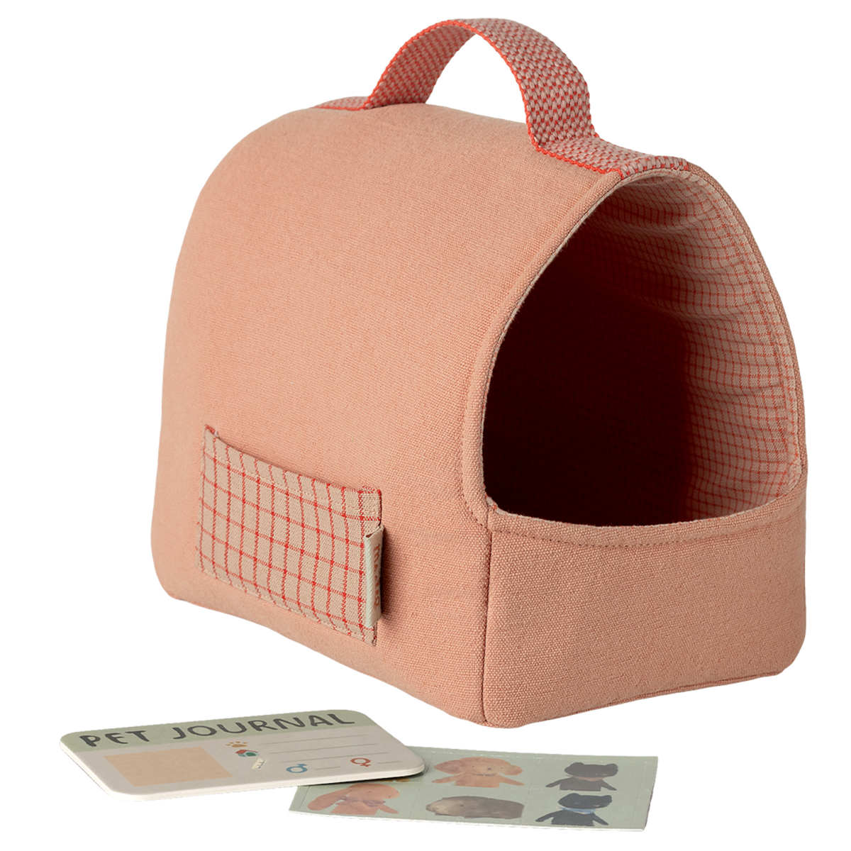 A soft, peach-colored pet carrier with a red grid pattern and handle. Nearby are a Pet Journal and dog stickers against a white background, conveying a cozy, playful vibe.